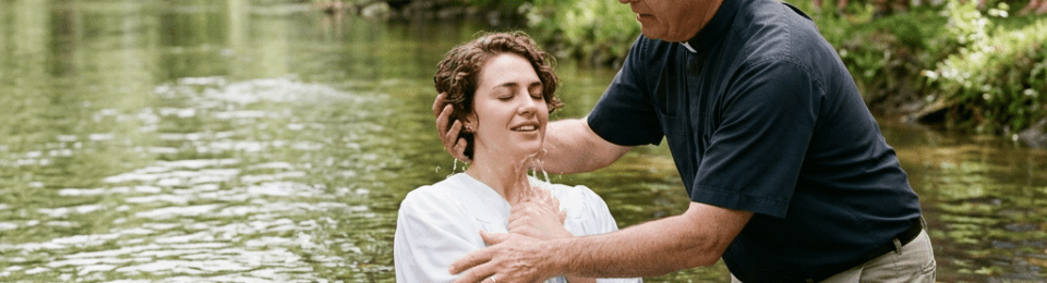 Clergy baptizing a person in a river with a group watching on the bank