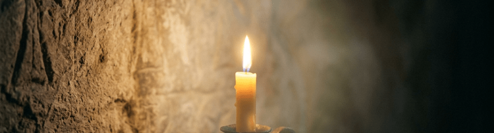 Lit candle in iron holder on wooden surface near carved stone wall
